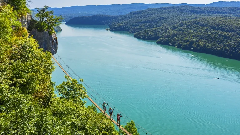 Traversée de la passerelle de 90 mètres avec vue sur le lac de Vouglans sur le parcours de la via ferrata du Regardoir à Moirans-en-Montagne dans le Jura.