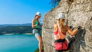 Une participante traverse sur le parcours de la via ferrata du Regardoir en bordure du lac de Vouglans dans le Jura avec une monitrice de la société Eskaleo.