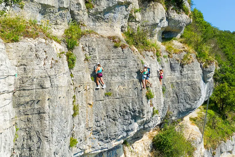 Un groupe de personnes accompagnées par un moniteur évoluent en traversée sur la via ferrata du Regardoir dans le Jura.
